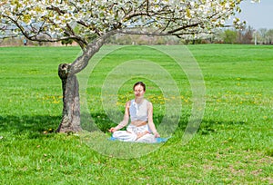 Beautiful woman is practicing yoga sitting in Lotus pose near blossom tree