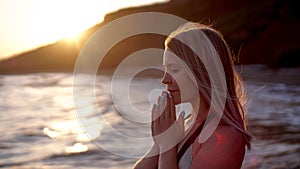 Beautiful woman prays on the sea shore on the sunset