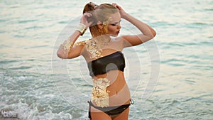 Beautiful woman with professional golden makeup standing in the water on the beach, looking in the camera.