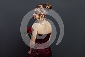 Beautiful woman profile and back head with blonde hairdo and red rose flower on black. Perfect model in red dress