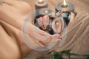 Beautiful woman with purifying black mask on her face. Beauty model girl with black facial peel-off mask lying in spa salon photo