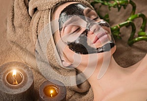 Beautiful woman with purifying black mask on her face. Beauty model girl with black facial peel-off mask lying in spa salon photo