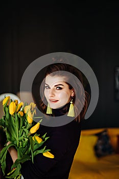 Beautiful woman in purple clothes with yellow flowers tulips in her hands on a dark background