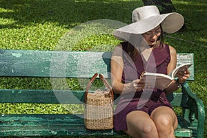 Beautiful woman, purple dress, sitting on a bench and reading in the garden
