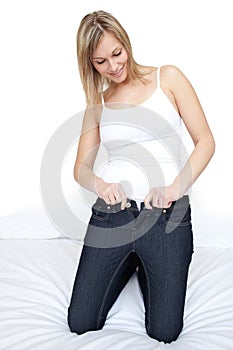 Beautiful woman putting on tight jeans on a bed