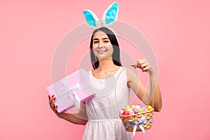 Beautiful woman in rabbit ears with a gift and a basket of colored eggs in her hands, a traditional holiday