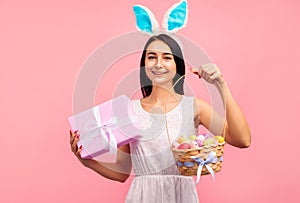 Beautiful woman in rabbit ears with a gift and a basket of colored eggs in her hands, a traditional holiday