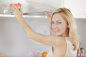 Beautiful woman reaching for crockery from kitchen cupboard