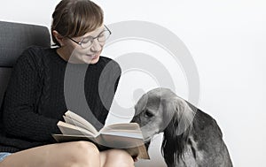 Beautiful woman reading book with her dog. greyhound sduty read