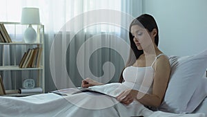 Beautiful woman reading glossy magazine with interest, pleasant pastime at home