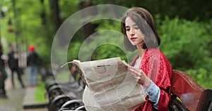 Beautiful woman reading newspaper in park. 4K video.