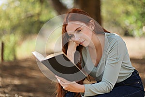 Beautiful woman reads a book sitting under the shade of a tree