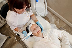 Beautiful woman receiving facial microcurrent treatment from beautician in beauty wellness salon . Microcurrent therapy