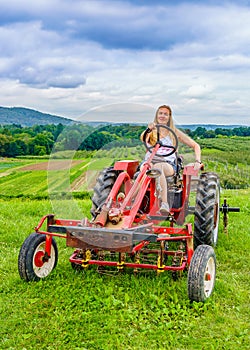 Beautiful woman on a red agricultural tractor, green field, landscape of meadow with grass Upstate New York