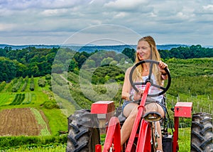 Beautiful woman on a red agricultural tractor, green field, landscape of meadow with grass Upstate New York