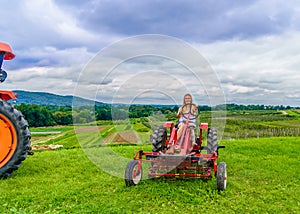 Beautiful woman on a red agricultural tractor, green field, landscape of meadow with grass Upstate New York