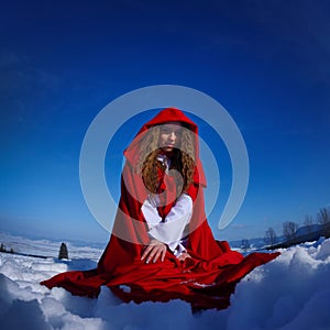 Beautiful woman with red cloak sitting on snow