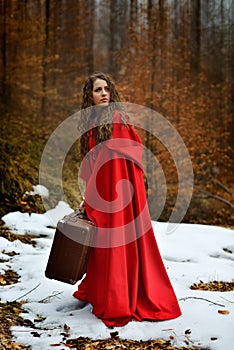 Beautiful woman with red cloak and suitcase alone in the woods