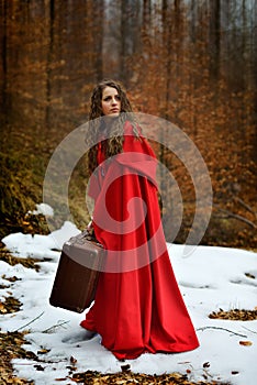 Beautiful woman with red cloak and suitcase alone in the woods photo