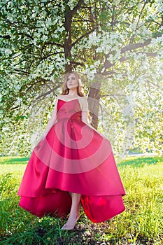 Beautiful woman in red dress on background of blossoming tree