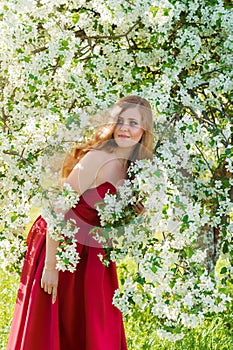 Beautiful woman in red dress with flowering tree in garden