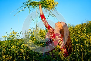 Beautiful woman in red dress holding bouquet of yellow flowers and enjoying summer sunny day in green field with green grass