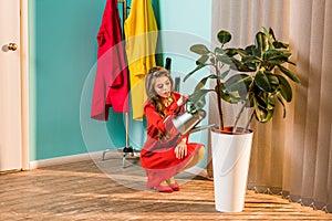 beautiful woman in red dress squatting and watering plant with watering can