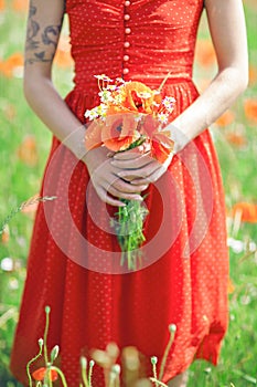 Beautiful woman in red dress standing in a poppy field holding flowers