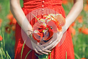 Beautiful woman in red dress standing in a poppy field holding flowers