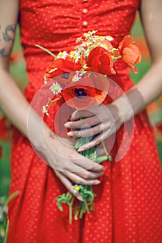 Beautiful woman in red dress standing in a poppy field holding flowers