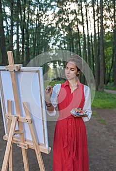 Beautiful woman in red dress in summer in park and forest, draws picture, creating creativity and creativity landscape