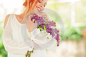 Beautiful woman with red hair holding white and violet lilac bloom in her hands, outdoor garden
