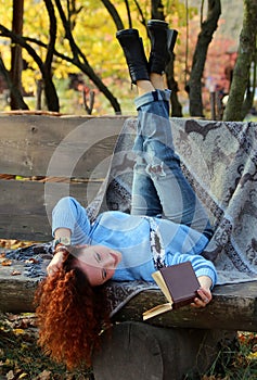 Beautiful Woman with red hair lying on a bench with a veil and reading a book.