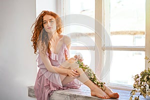 Beautiful woman with red hair sitting at the window with flowers, spring mood