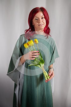 Beautiful woman with red hair in yellow dress on a light background holds tulips. Inernational woman's day 8 March