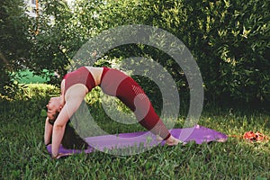 Beautiful woman in red leggings and a top practicing yoga in a city park