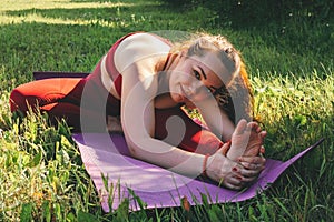 Beautiful woman in red leggings and a top practicing yoga in a city park