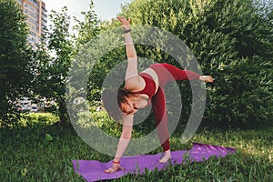 Beautiful woman in red leggings and a top practicing yoga in a city park