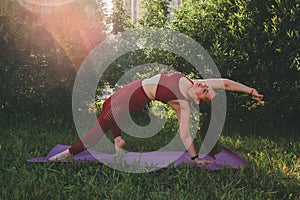 Beautiful woman in red leggings and a top practicing yoga in a city park