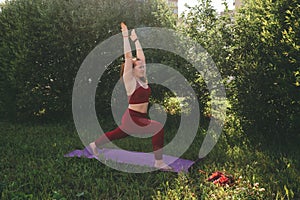 Beautiful woman in red leggings and a top practicing yoga in a city park