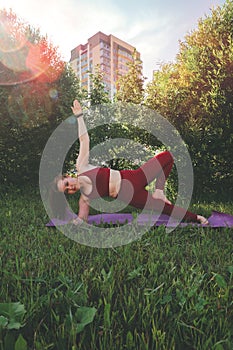 Beautiful woman in red leggings and a top practicing yoga in a city park
