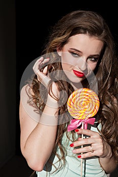 Beautiful woman with red lips eats a big candy sweet lollipop