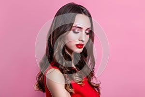 Beautiful woman with red lips, makeup and hairstyle in red dress on pink background