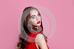 Beautiful woman with red lips, makeup and hairstyle in red dress on pink background