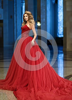 Beautiful woman in a red long dress and a golden crown in the gr