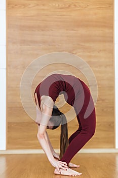 Beautiful woman in red sportswear practices backbend yoga asana Urdhva Dhanurasana - Upward facing bow pose at the yoga studio.