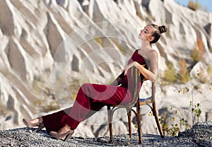 A beautiful woman relaxes on a chair in a red jumpsuit near the white mountains