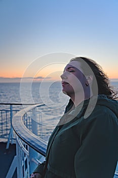 Beautiful woman relaxing against the boat balcony railing with closed eyes and the wind in her hair