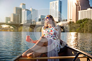 Beautiful woman relaxing on a boat, summer day on lake with city skyscrapers in background, commercial travel concept