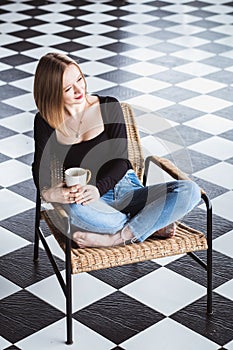 Beautiful woman relaxing in a comfortable chair with cup of coffee in lotus position against black and white background